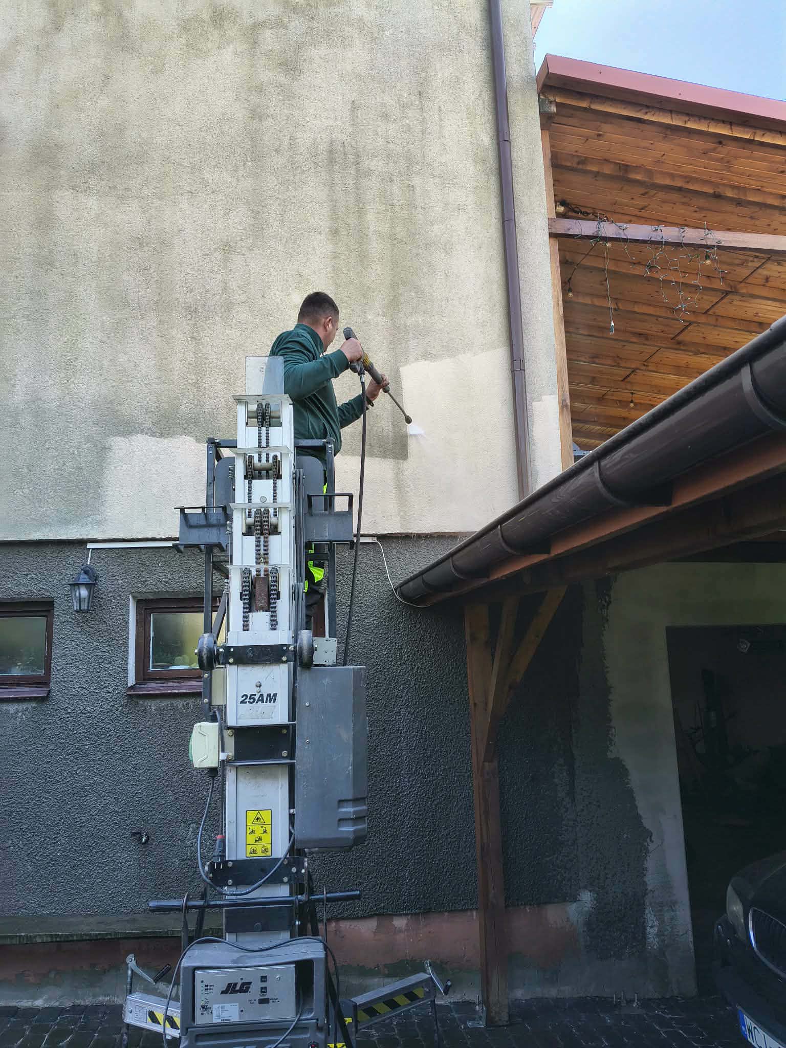 Operator na podnośniku myjący ścianę domu