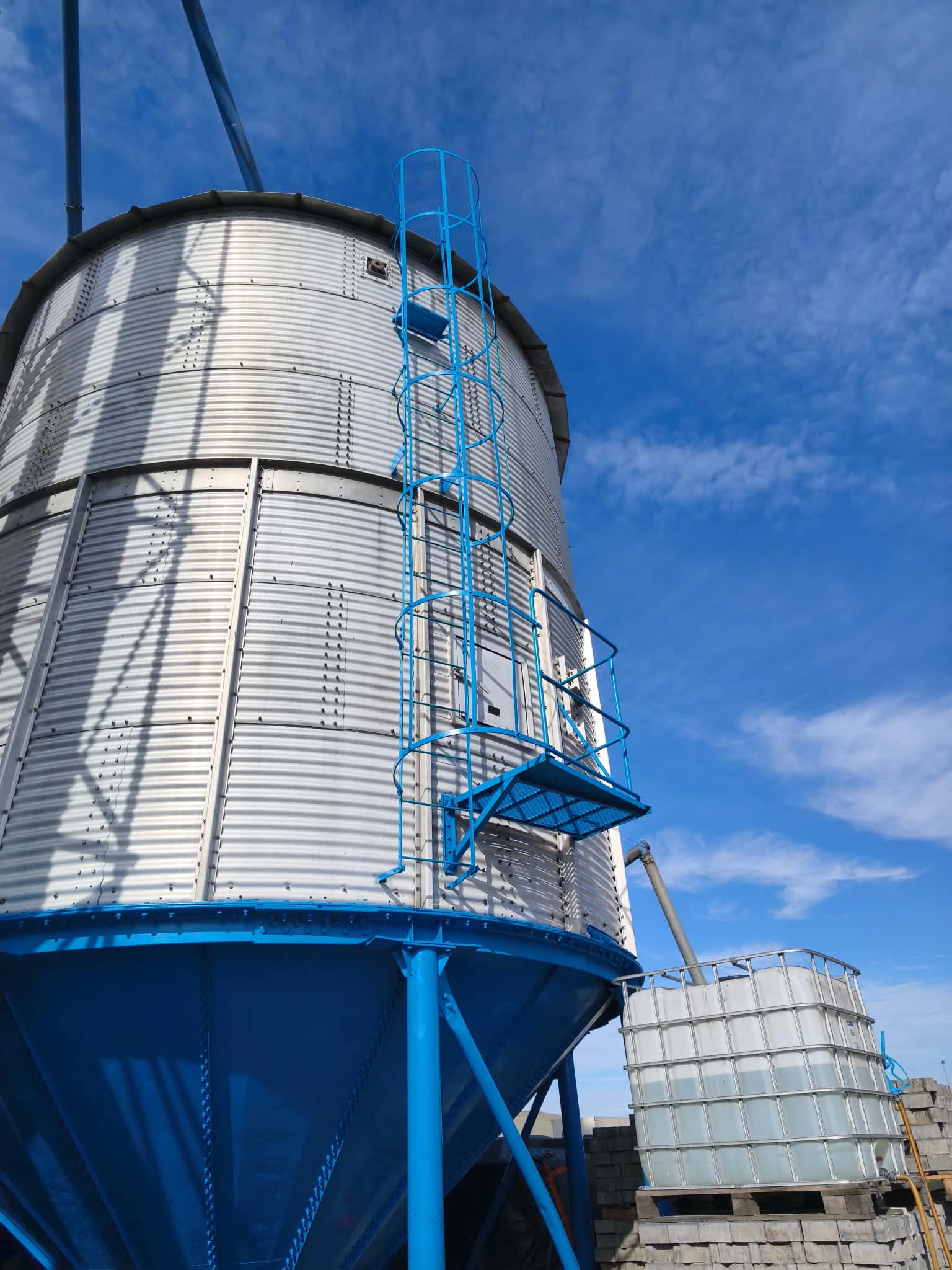 Wysoki metalowy silos z odnowioną niebieską konstrukcją na tle nieba